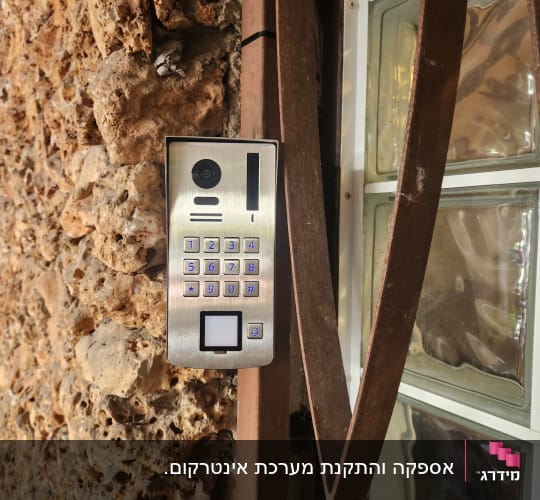מערכת אינטרקום מותקנת על קיר אבן ליד חלון זכוכית